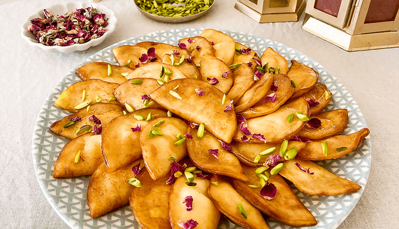 qatayef with cream garnished with pistachios and rose petals served on plate